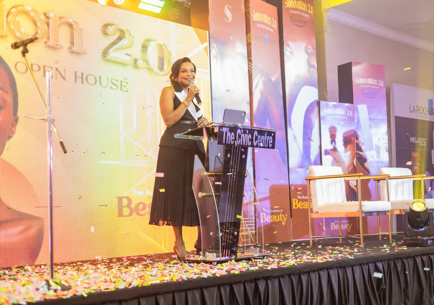 Dr. Uzo speaks onstage at a Skinovation 2.0 with microphone and podium.